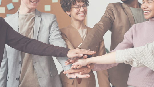 Team von Menschen mit übereinandergelegten Händen – Symbol für Zusammenarbeit und Teamarbeit