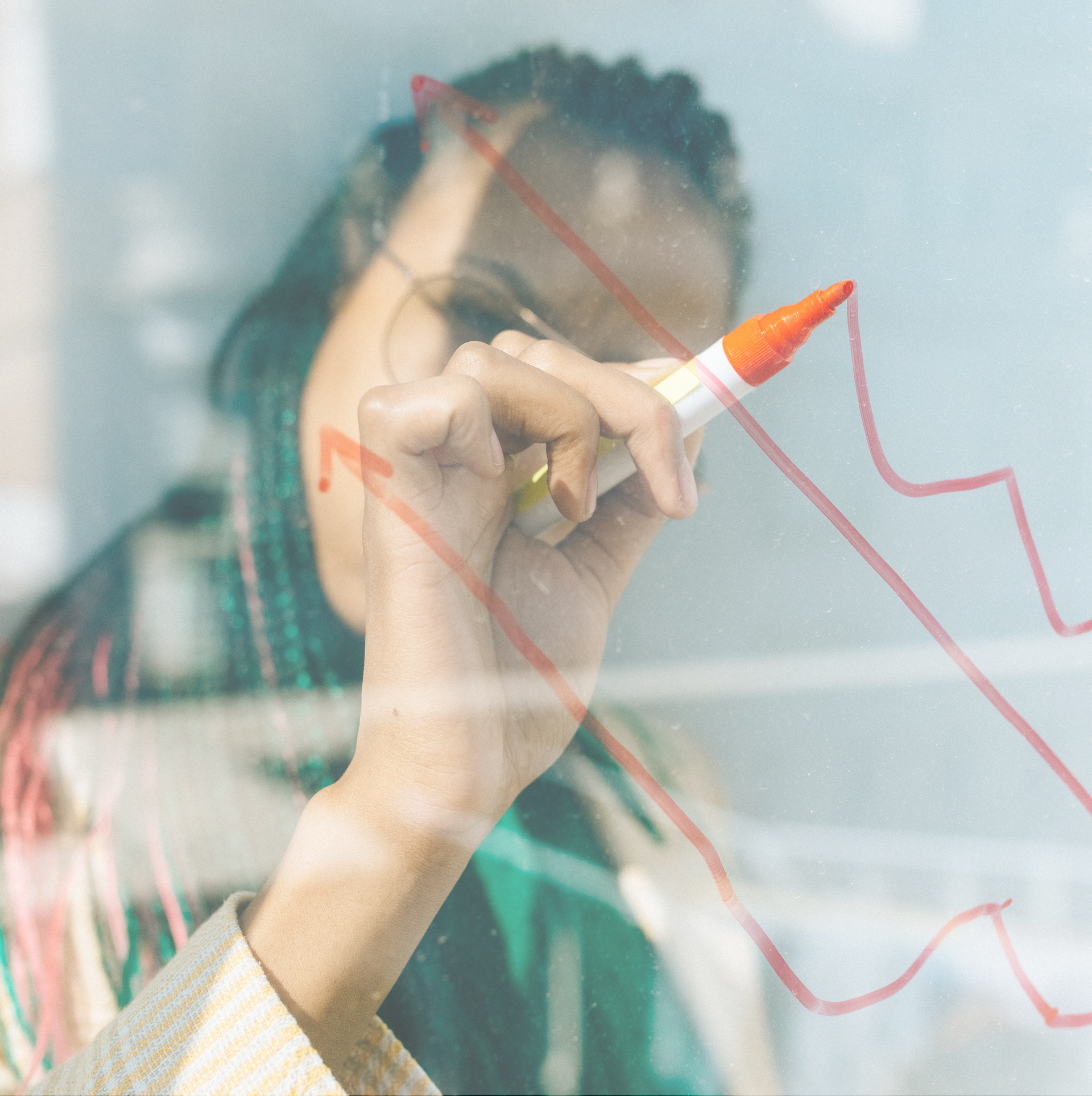 Frau zeichnet mit einem Stift ein Diagramm auf eine Glasscheibe – Symbol für Strategie und Planung