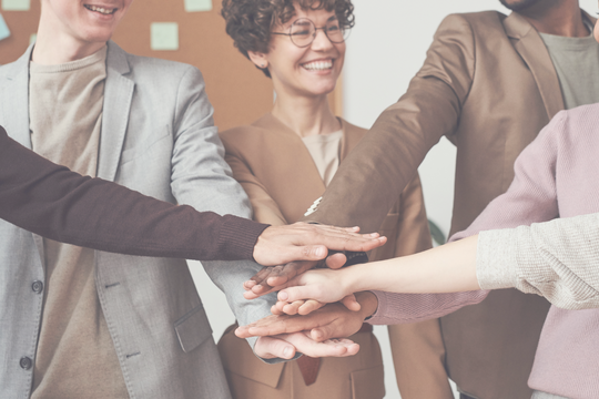 Team von Menschen mit übereinandergelegten Händen – Symbol für Zusammenarbeit und Teamarbeit